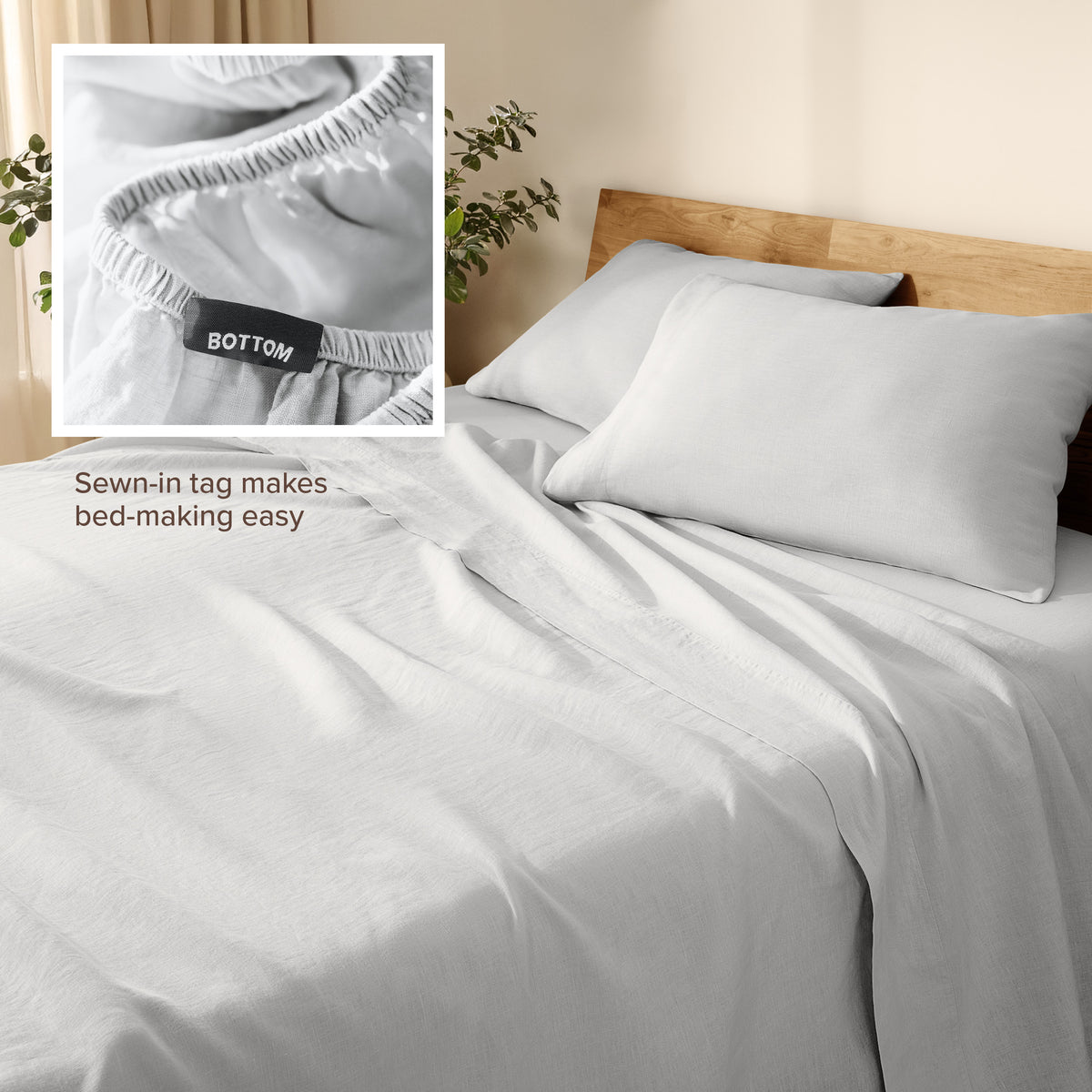 Linen bed sheets and pillowcases on a wooden bed with a plant in the background