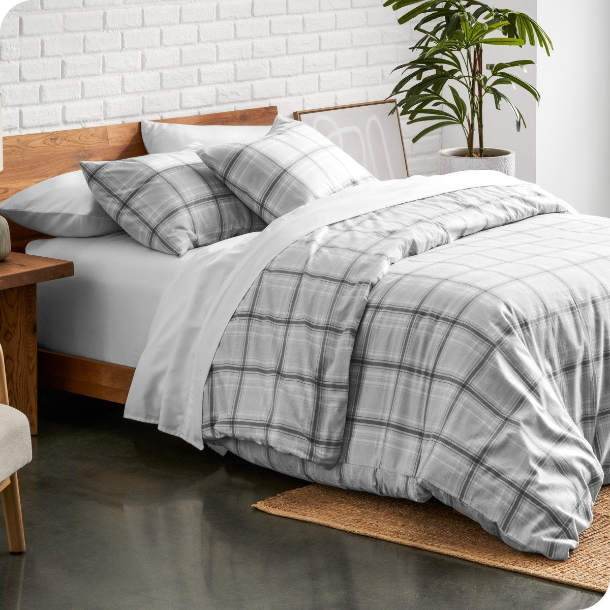 Bed with plaid bedding in a bedroom setting with a plant and wooden side table.
