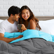 Man and woman sitting on a bed holding a mug, smiling at each other.