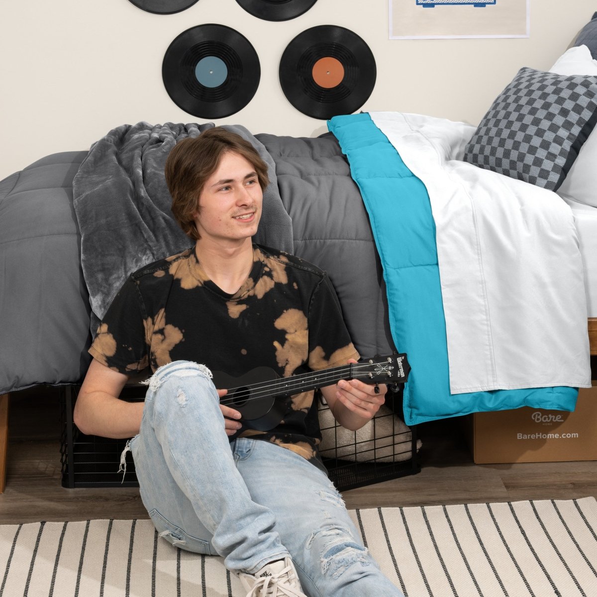 Person sitting on a bed holding a guitar in a bedroom setting with vinyl records on the wall.