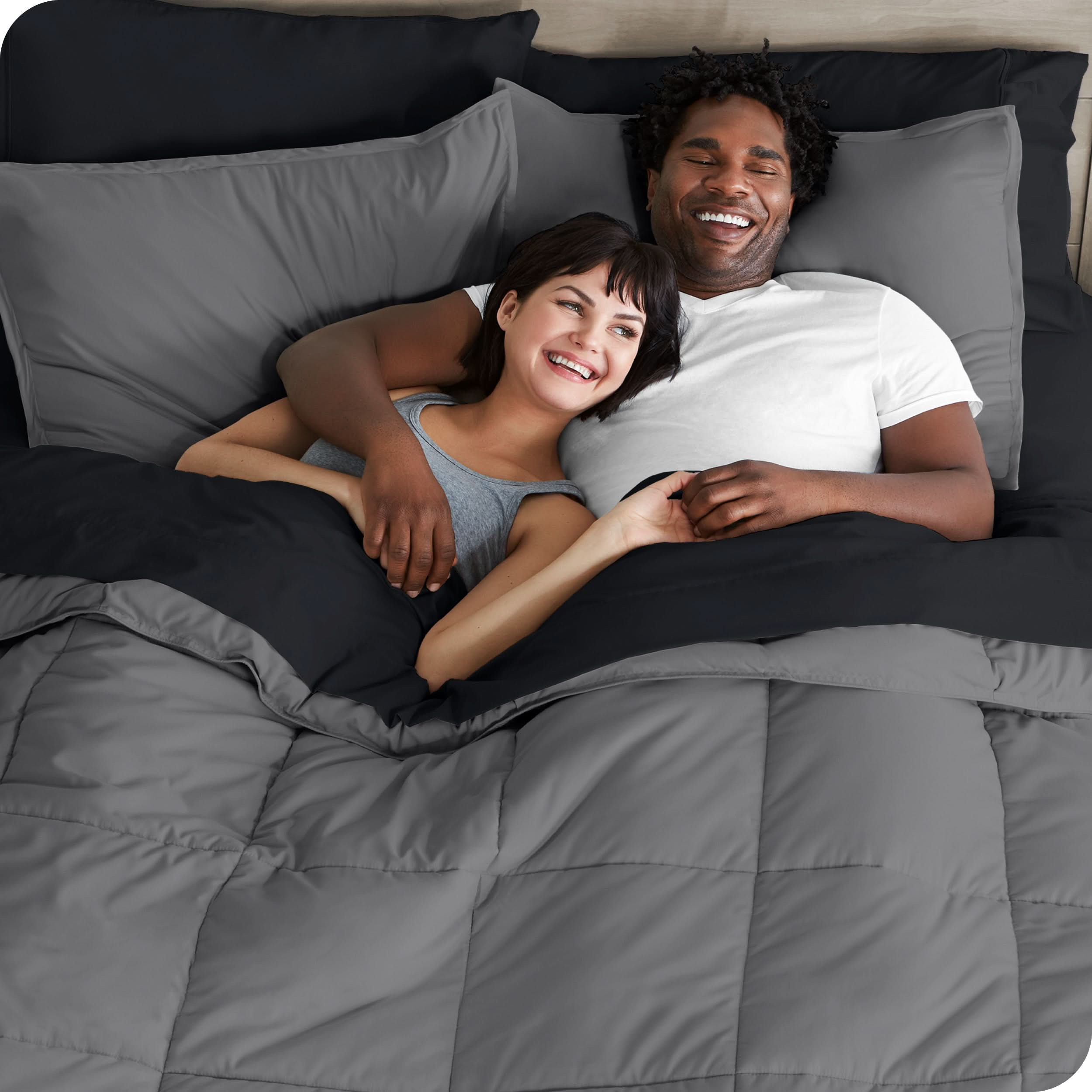 A couple is lying in bed with a comforter and sheets over them