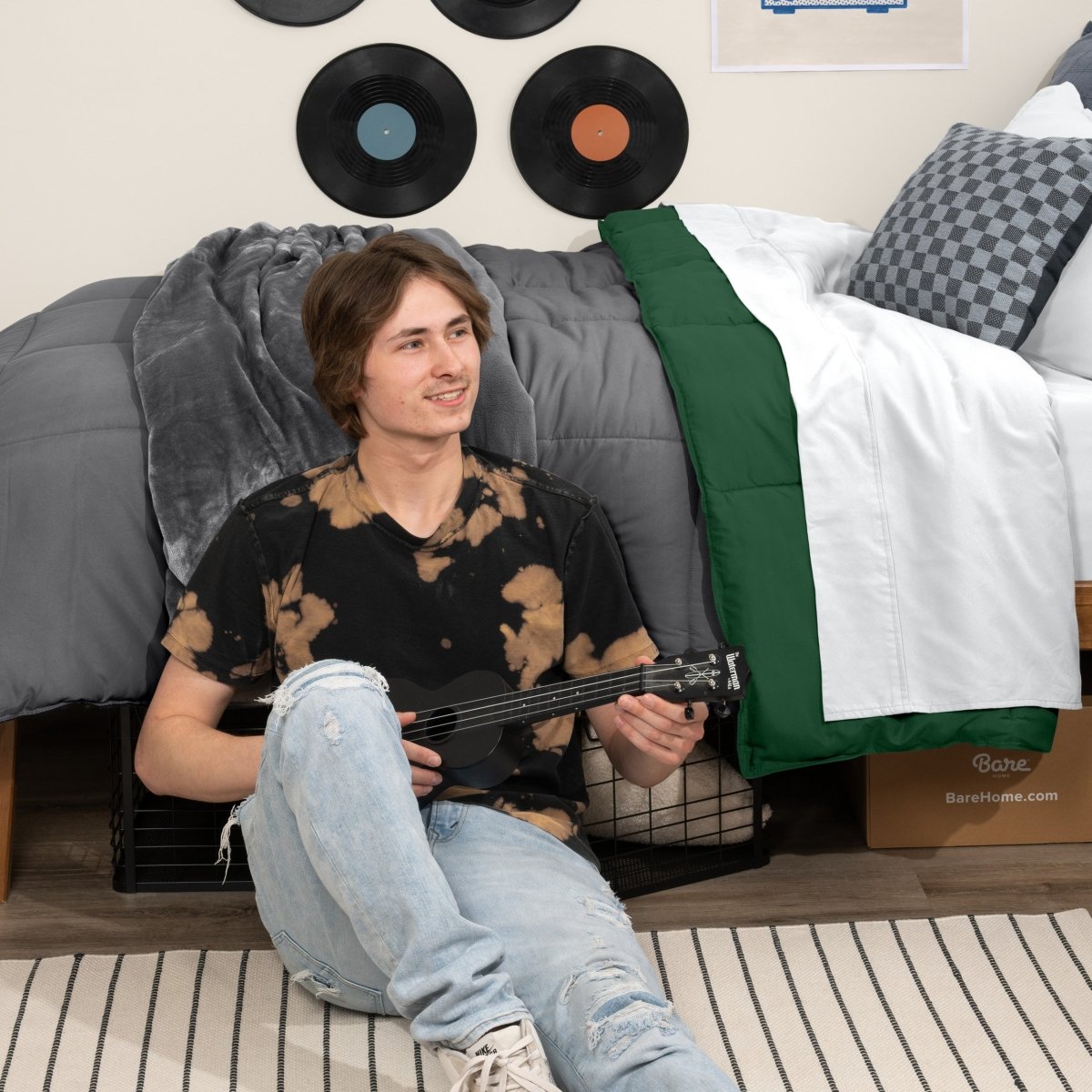 Person sitting on a bed holding a guitar in a bedroom setting with vinyl records on the wall.