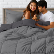 A couple sitting in a bed made with a reversible comforter and sheet set