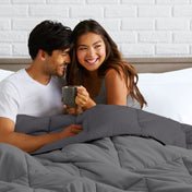 Man and woman sitting on a bed holding a mug, smiling at each other.