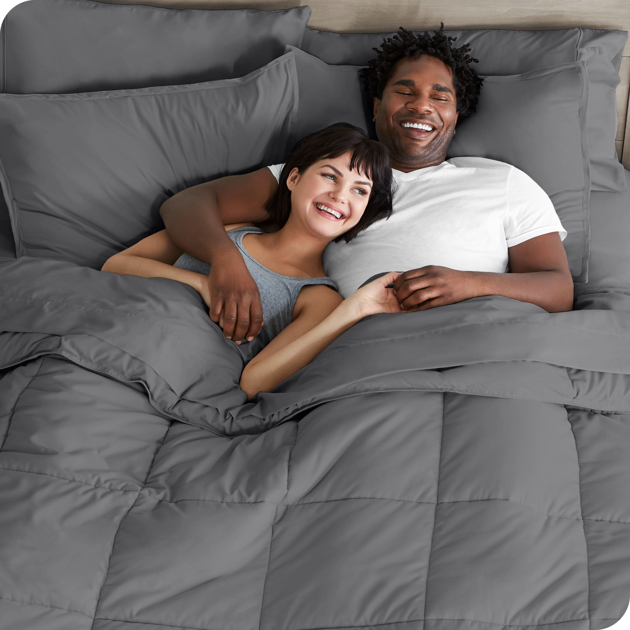 A couple is lying in bed with a comforter and sheets over them