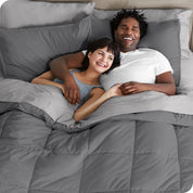 A couple is lying in bed with a comforter and sheets over them