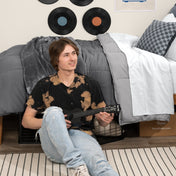 Person sitting on a bed holding a guitar in a bedroom setting with vinyl records on the wall.