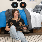 Person sitting on a bed holding a guitar in a bedroom setting with vinyl records on the wall.