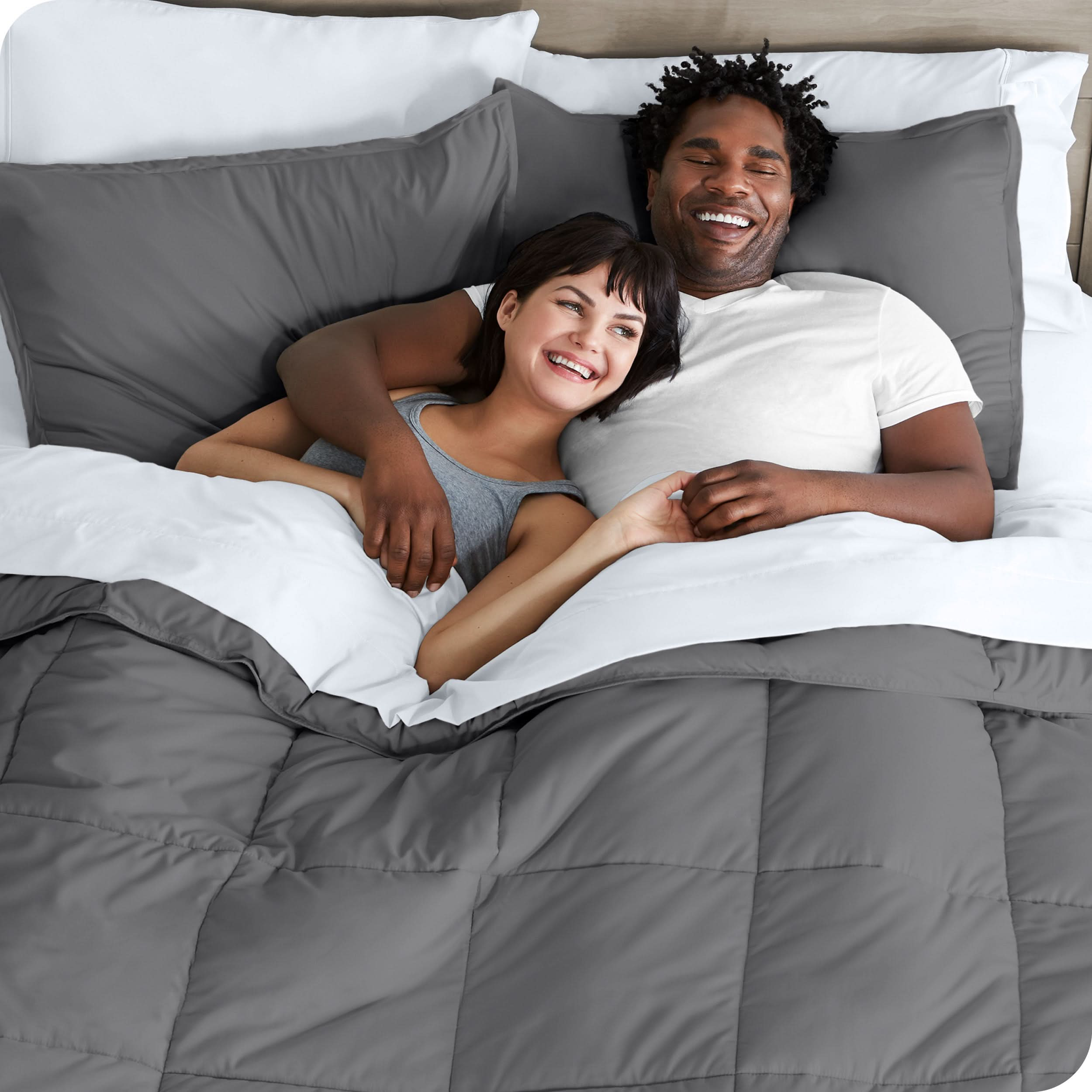 A couple is lying in bed with a comforter and sheets over them