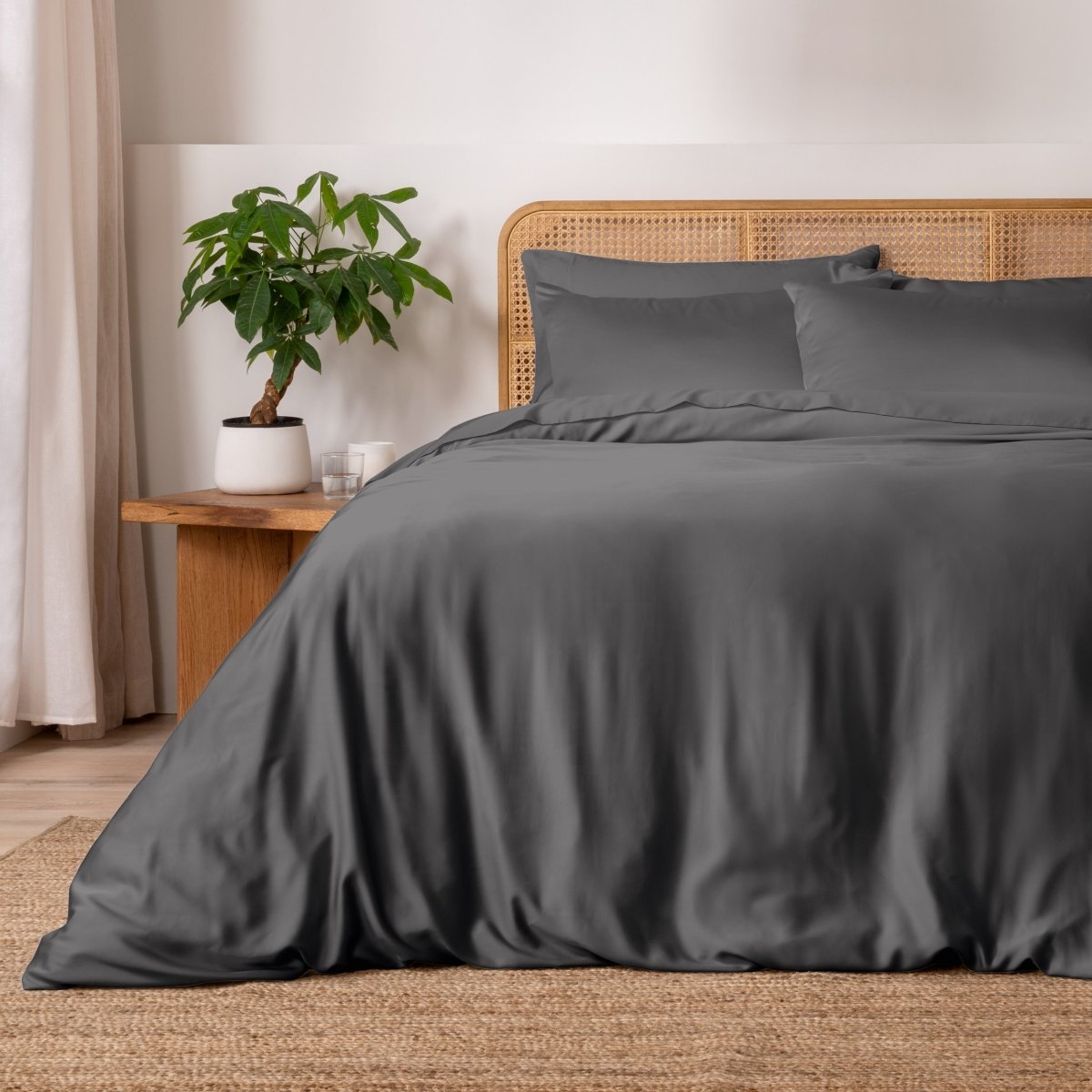 Gray bedding set on a bed with a wicker headboard and plant in the background.