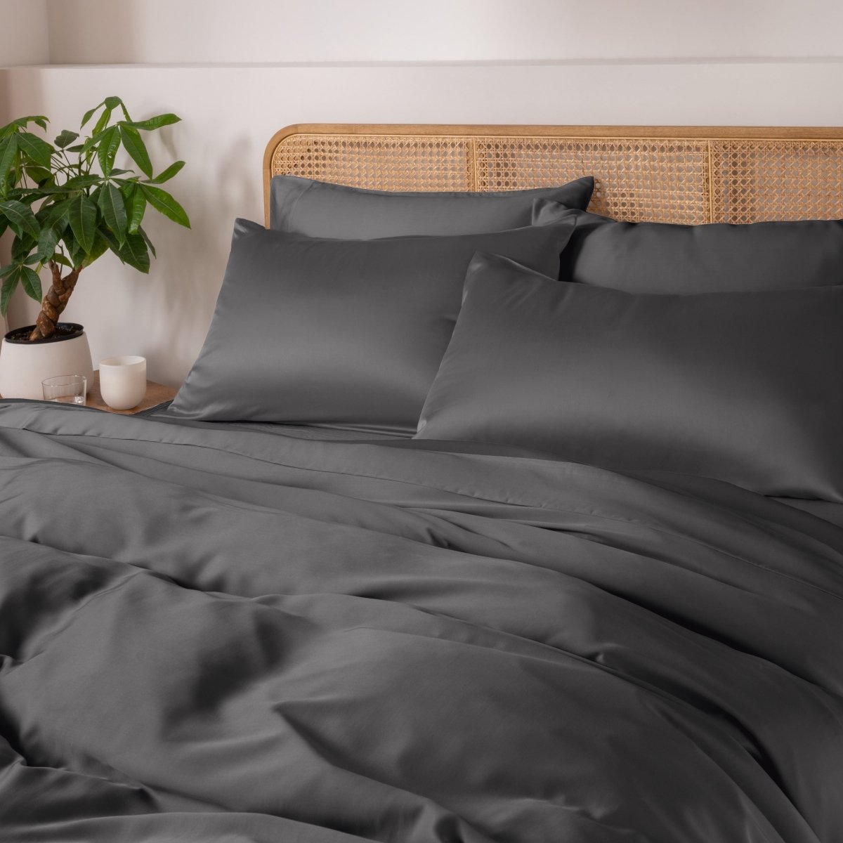 Gray bedding set on a bed with a wicker headboard and plant in the background.
