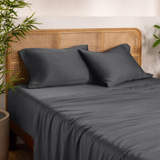 Bamboo bed sheets and pillows on a bed with a wicker headboard in a room with plants.