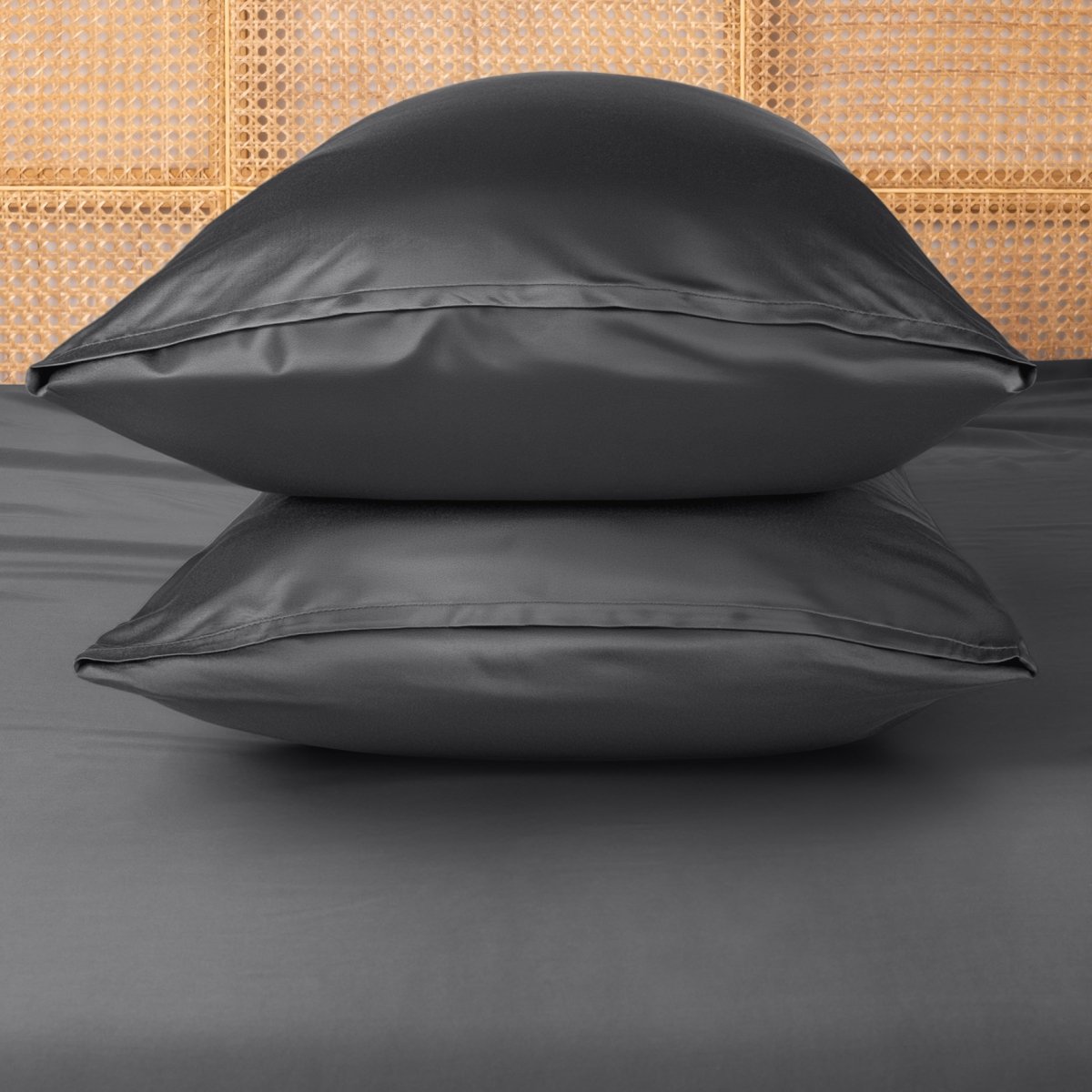 Two grey pillows stacked on a bed with a woven headboard.