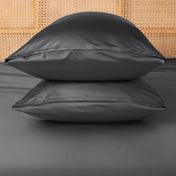 Two grey pillows stacked on a bed with a woven headboard.