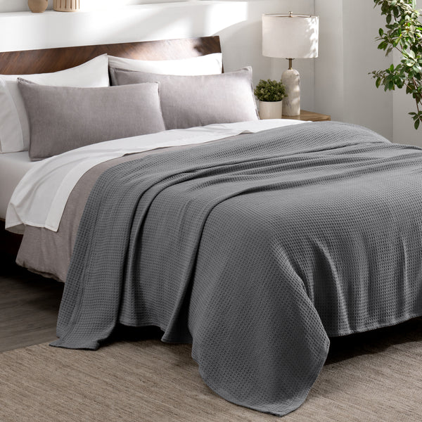 Cotton waffle blanket draped over a bed with pillows in a bedroom setting.
