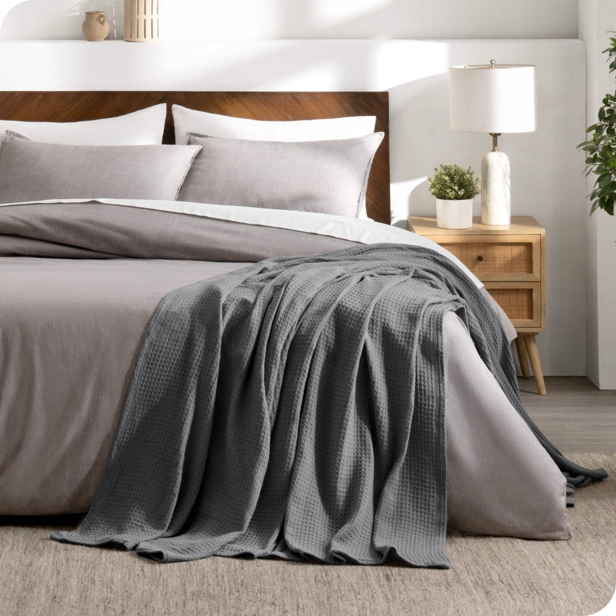A cotton waffle blanket is on the corner of a bed. It is hanging down the side and end of the bed.