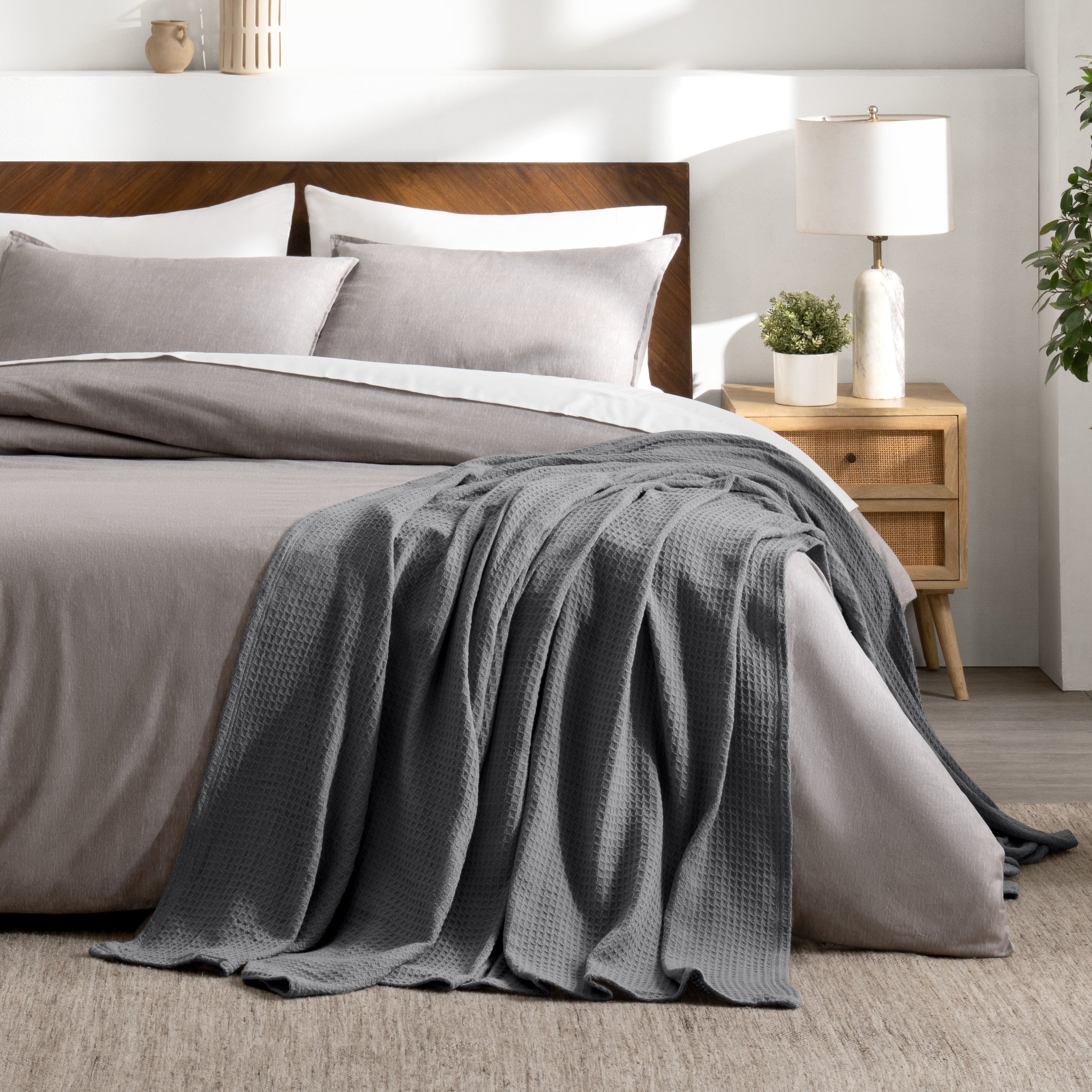 Bed with gray bedding and a throw blanket in a bedroom setting.