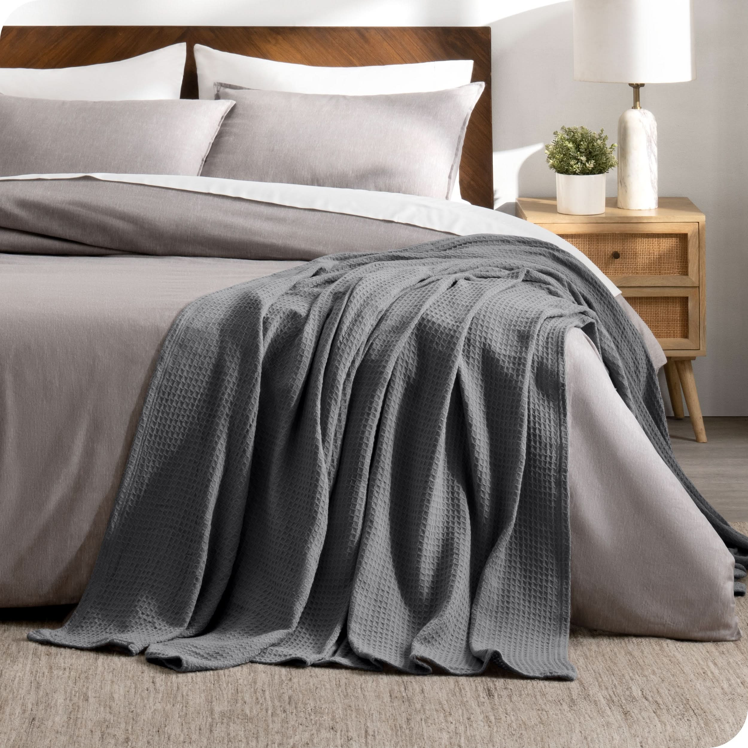 A cotton waffle blanket is on the corner of a bed. It is hanging down the side and end of the bed.