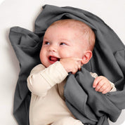 A baby lying on a receiving blanket. She has her thumb in her mouth.