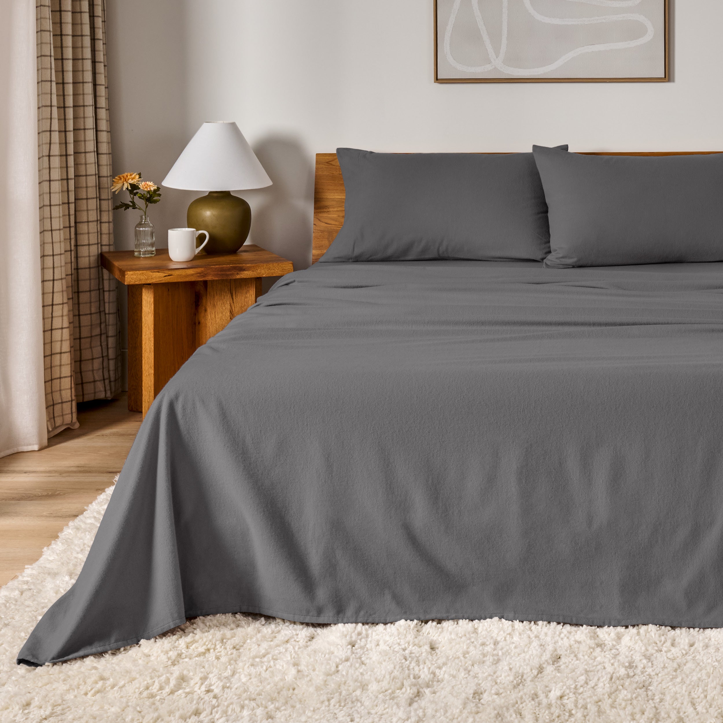 A bed dressed in flannel sheet set in a bedroom with a wooden headboard, bedside table and lamp