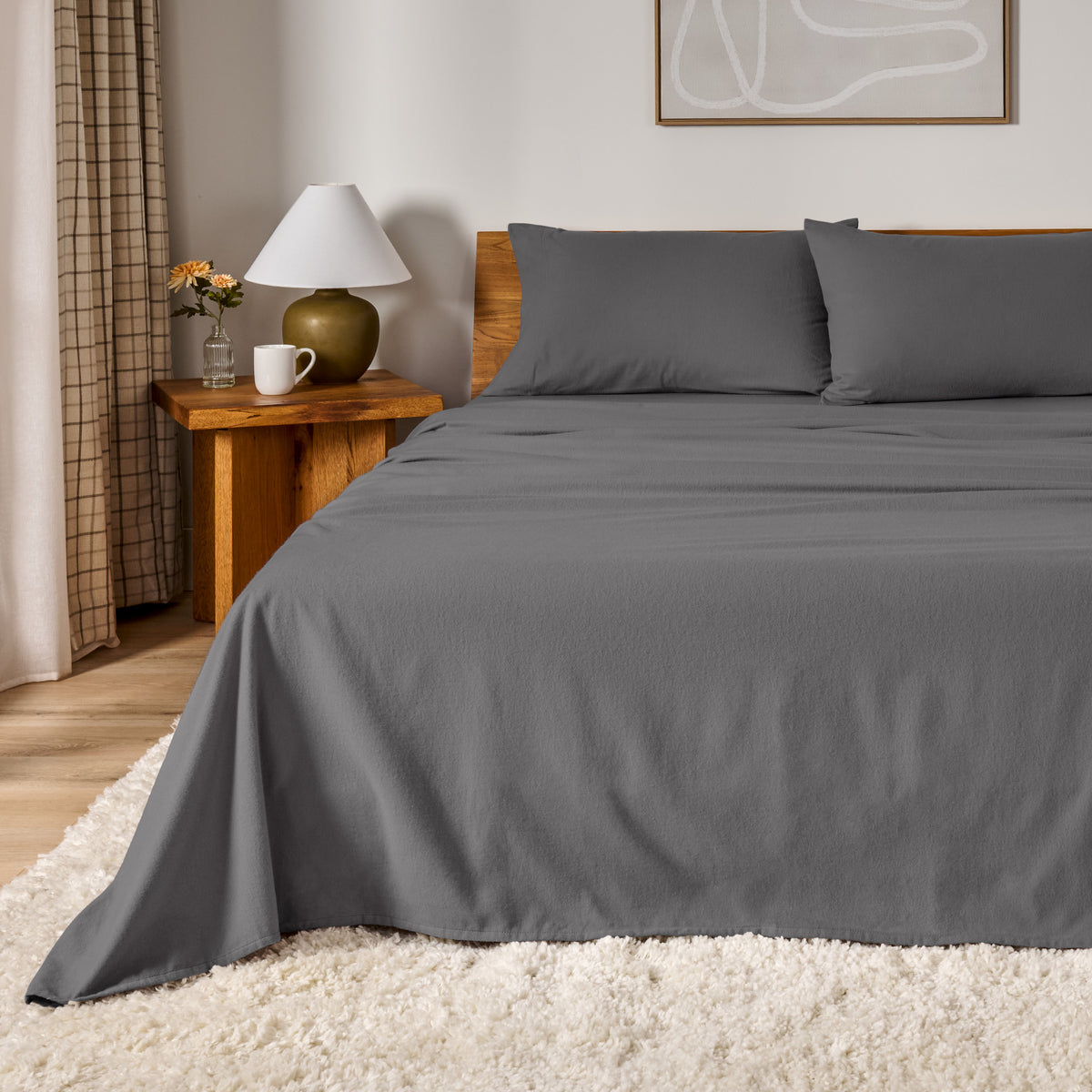A bed dressed in flannel sheet set in a bedroom with a wooden headboard, bedside table and lamp