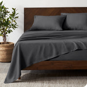 Dark wooden bed frame with grey linen sheets on the mattress