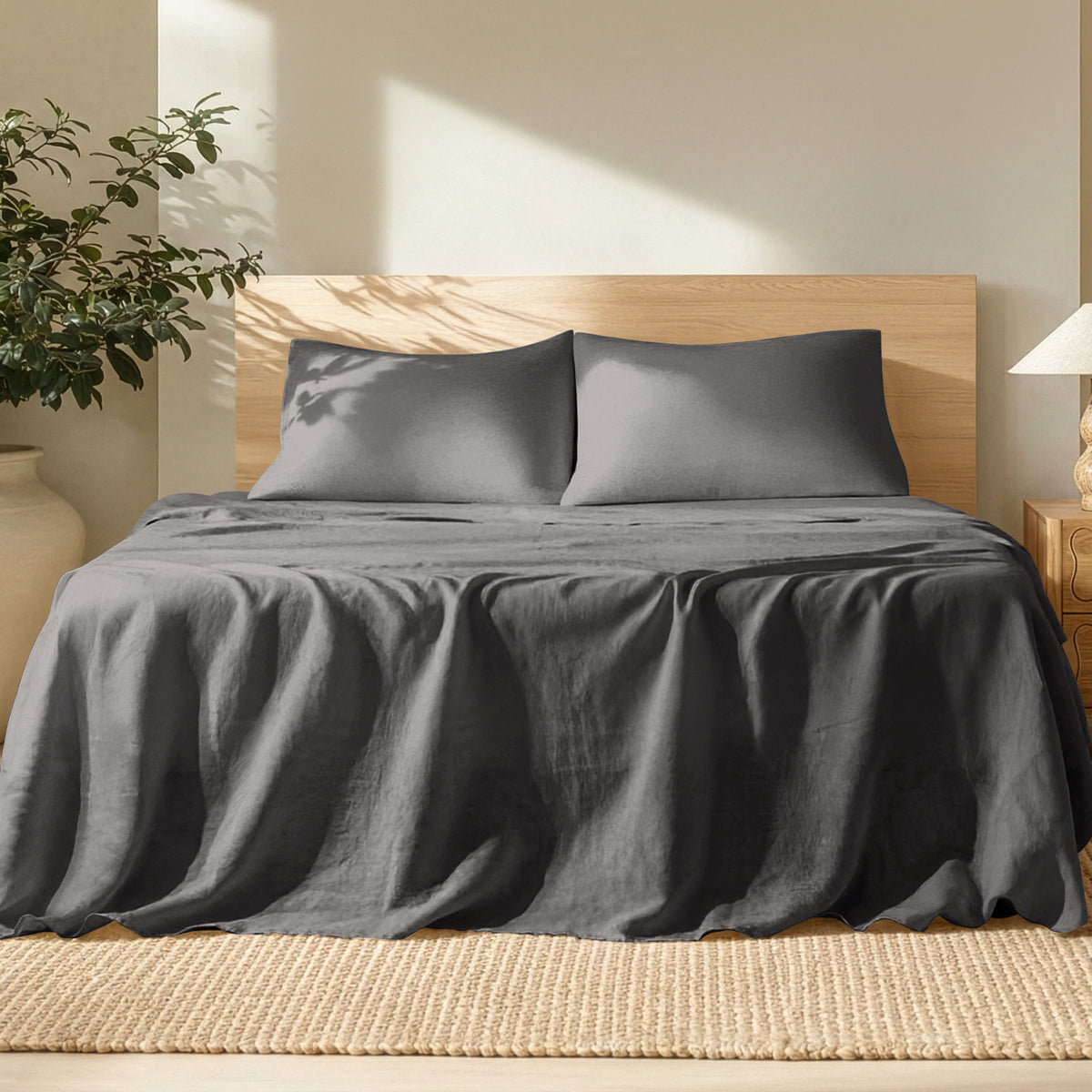 Bed with linen bedding and pillows in a bright room with a plant and lamp.