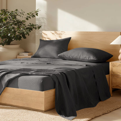 Bedroom with wooden bed frame, linen bedding, and a plant on a nightstand.