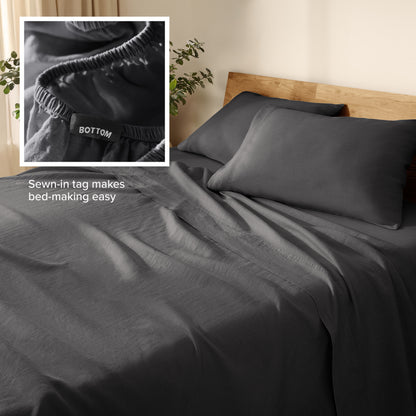 Linen bed sheets and pillowcases on a wooden bed with a plant in the background