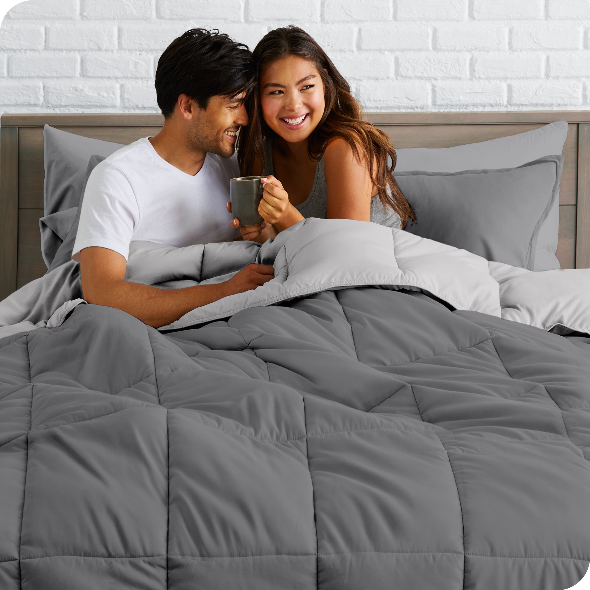 A couple sitting in a bed made with a reversible comforter and sheet set