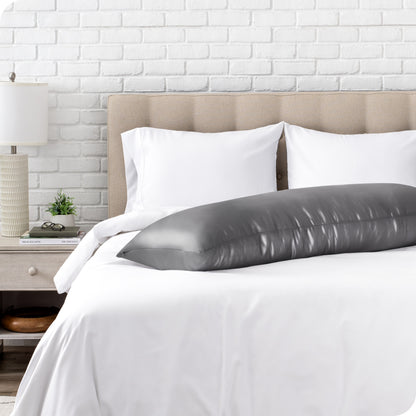 Bed with white bedding and a body pillow against a white brick wall.