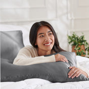 Woman lying on a bed with a body pillow, smiling.