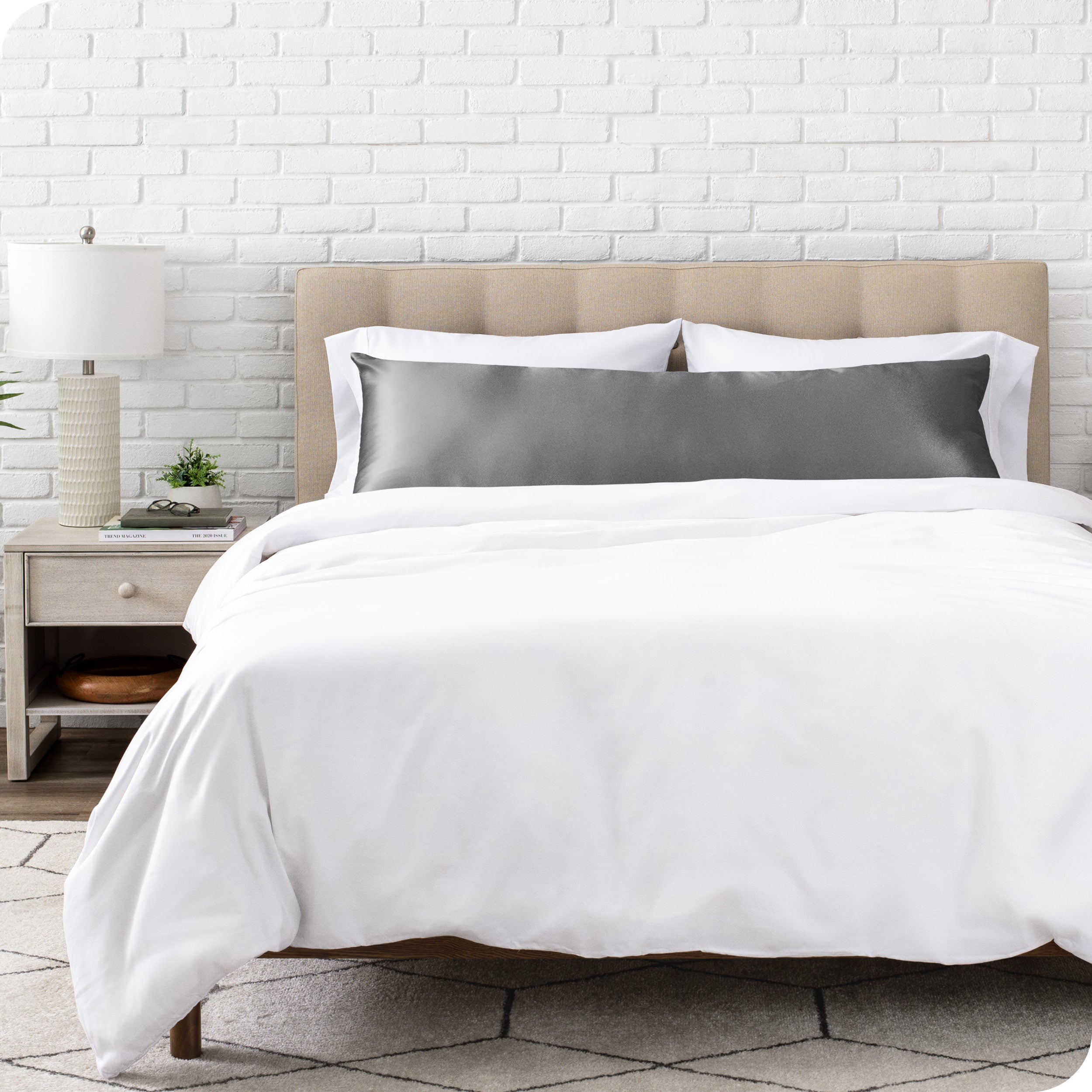 White bedding set with body pillow covered with a silk pillowcase on a bed in a bedroom setting.