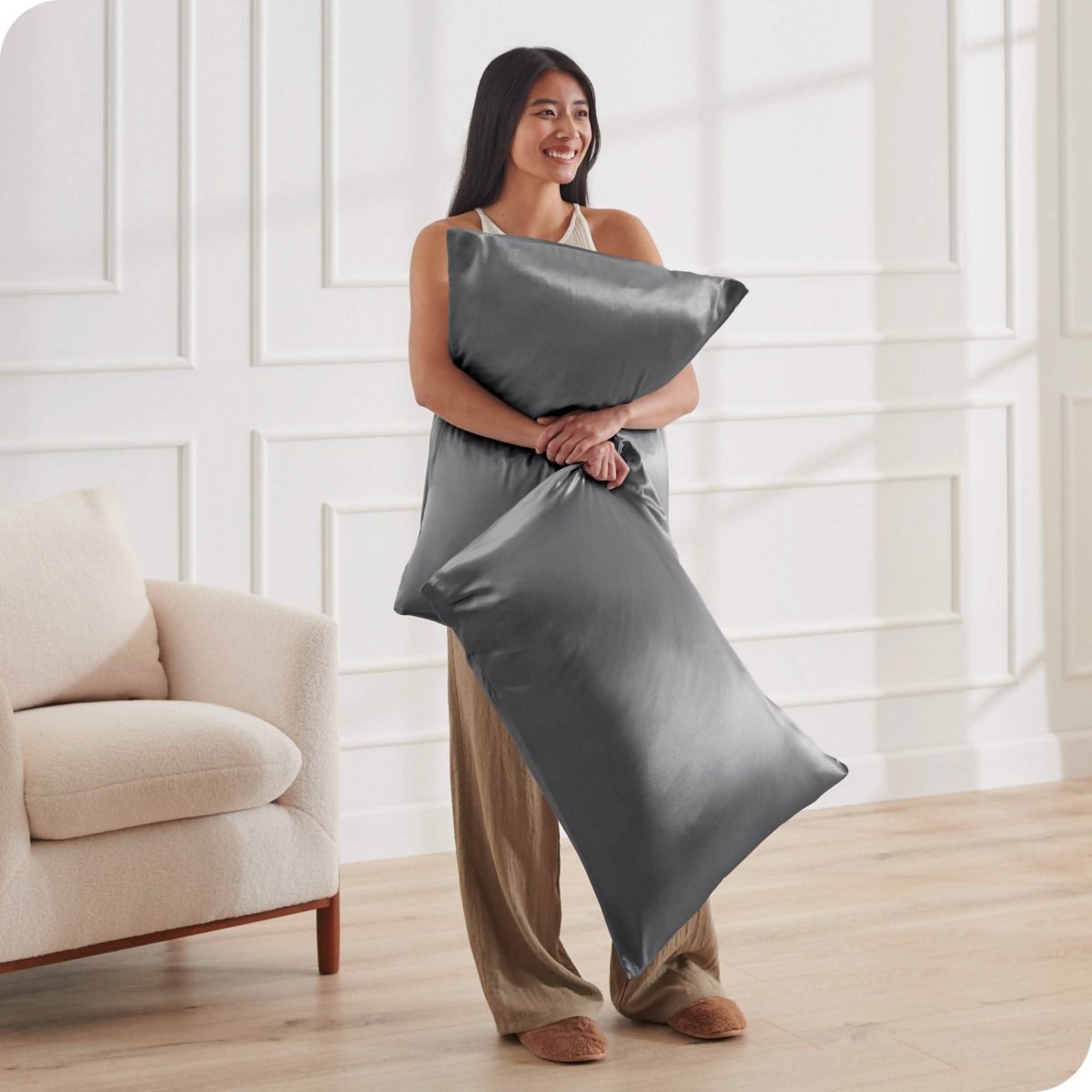 A woman standing while holding pillows with silk pillowcases on them