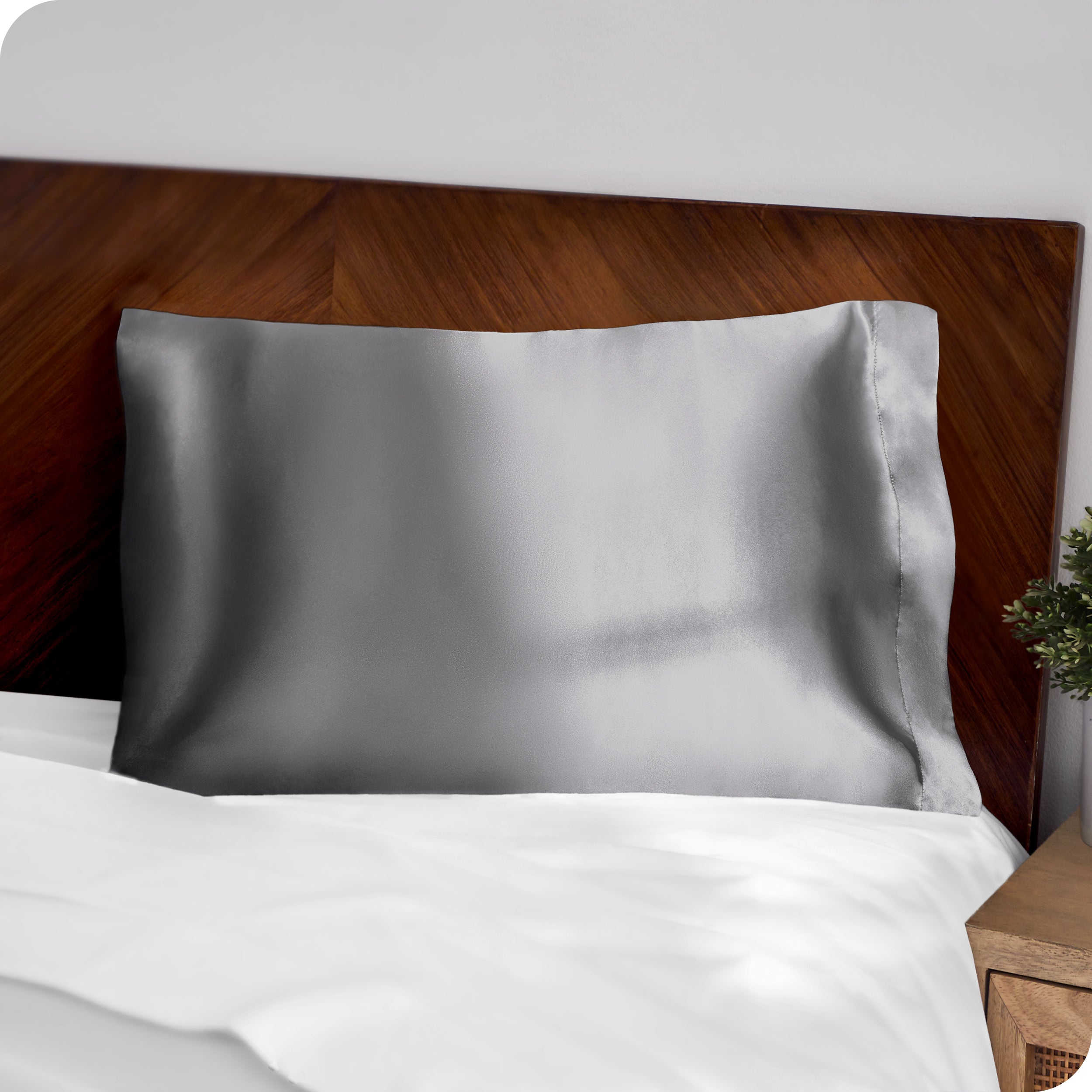 A grey silk pillowcase on a pillow resting on a headboard