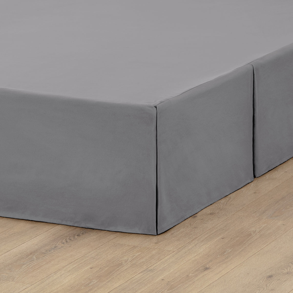 The corner of a box spring with a pleated bed skirt on it