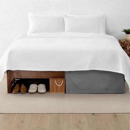 One side of a bed has shoes and a box under it while the other side has a bed skirt so that under the bed is hidden from view