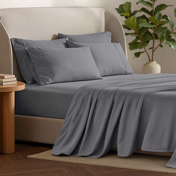 Bed sheets and pillows on a bed with a plant and side table in the background.