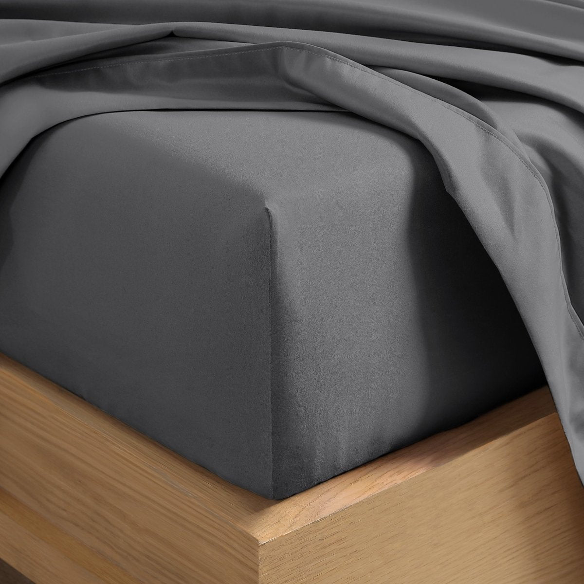 A close-up of a fitted sheet covering the corner of a bed frame, with matching top sheet draped over it.
