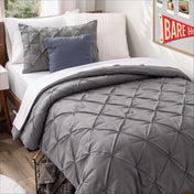 A college dorm bed dressed in a gray pintuck comforter set with extra pillows.
