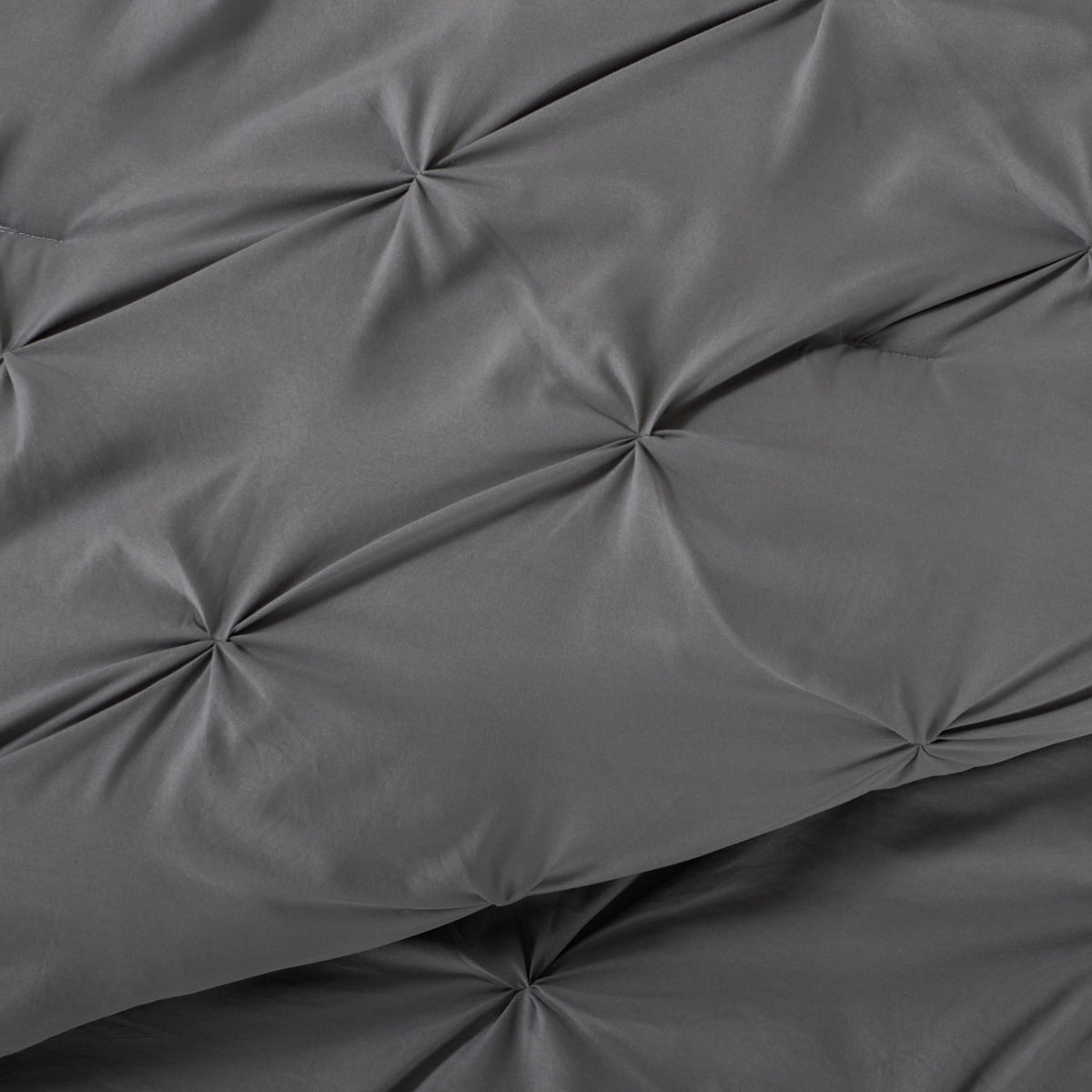 Gray pintuck comforter on a bed with a nightstand and lamp in the background