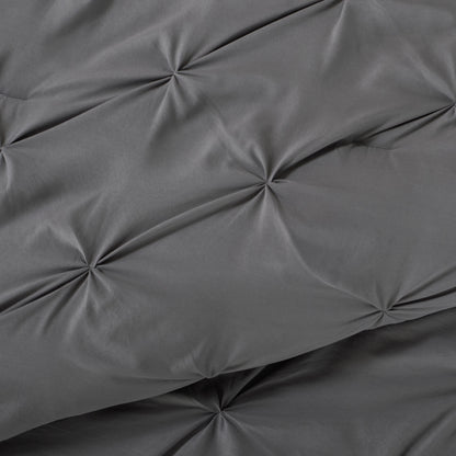Gray pintuck comforter on a bed with a nightstand and lamp in the background