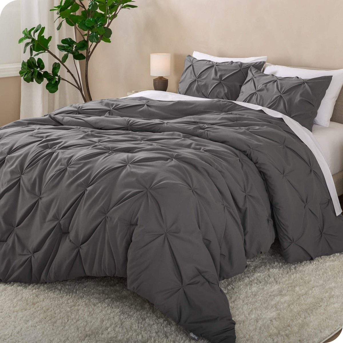 A side view of a bed with a grey pintuck comforter set draped over it