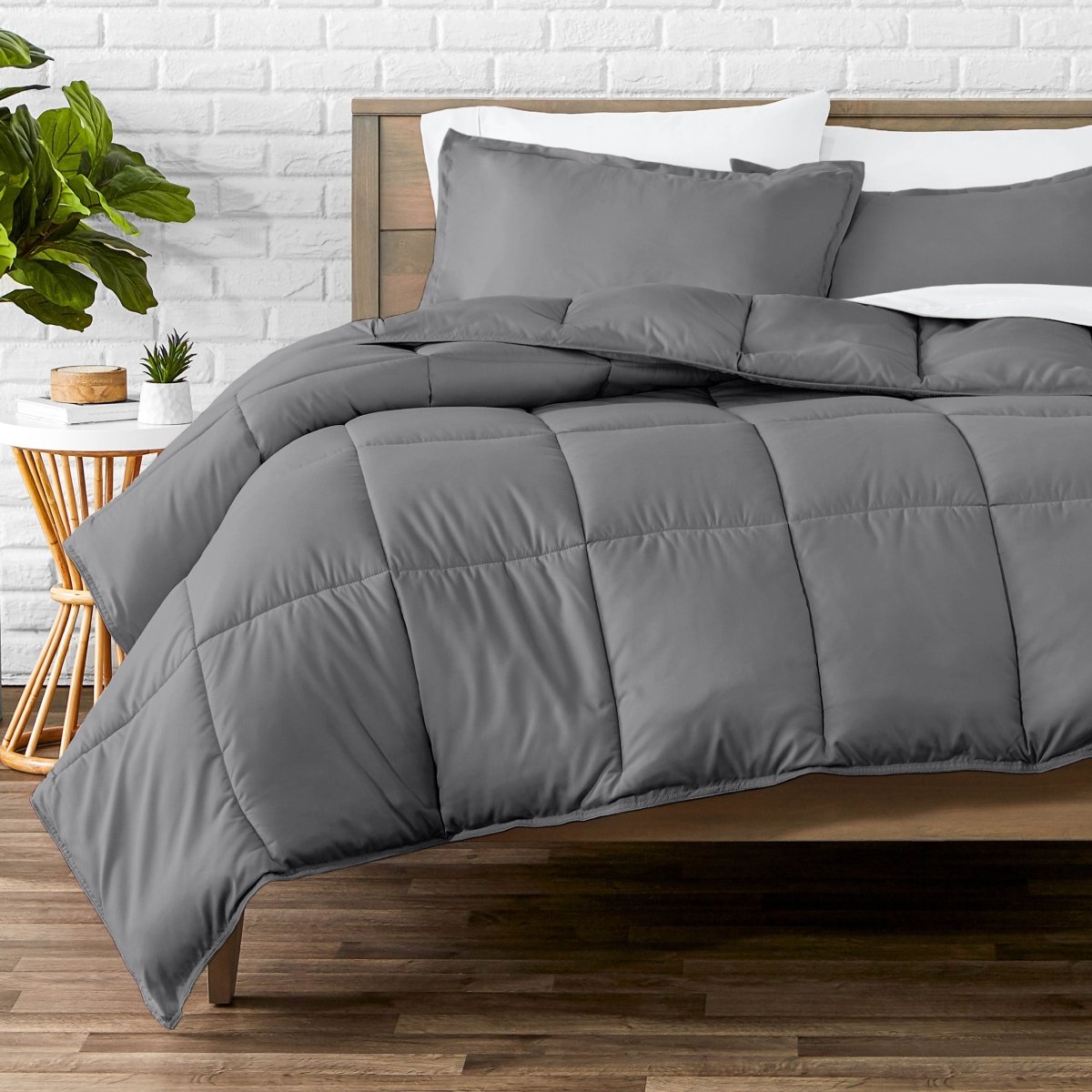 Comforter set on a bed with a white brick wall and plant in the background