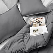 Comforter and pillows on a bed with a magazine and glasses.