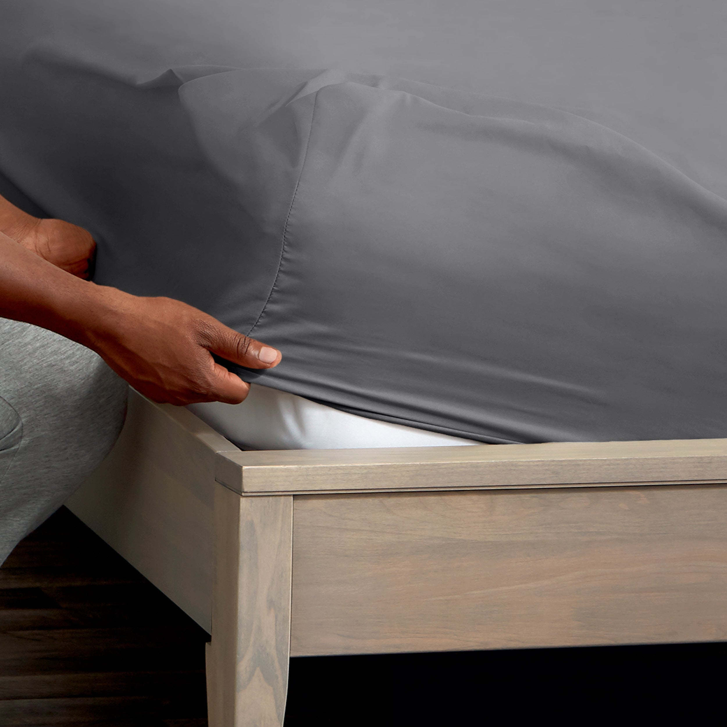 A man is putting a fitted sheet on a bed