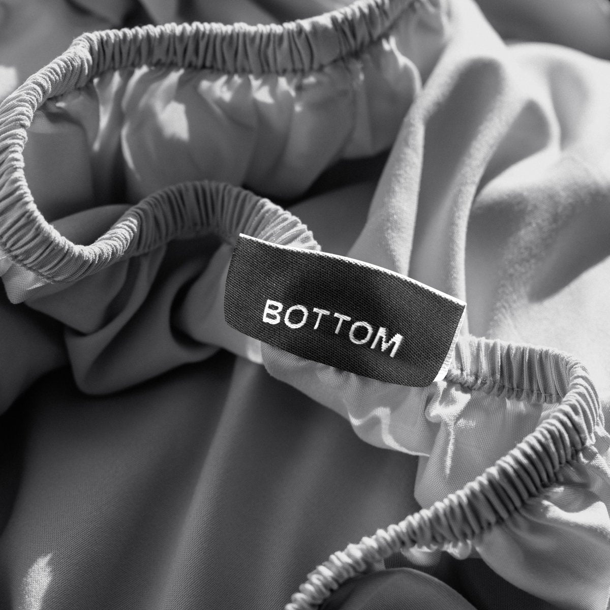 A close-up of a fitted sheet with a label printed with the word 'BOTTOM' in white.