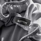 A close-up of a fitted sheet with a label printed with the word 'BOTTOM' in white.