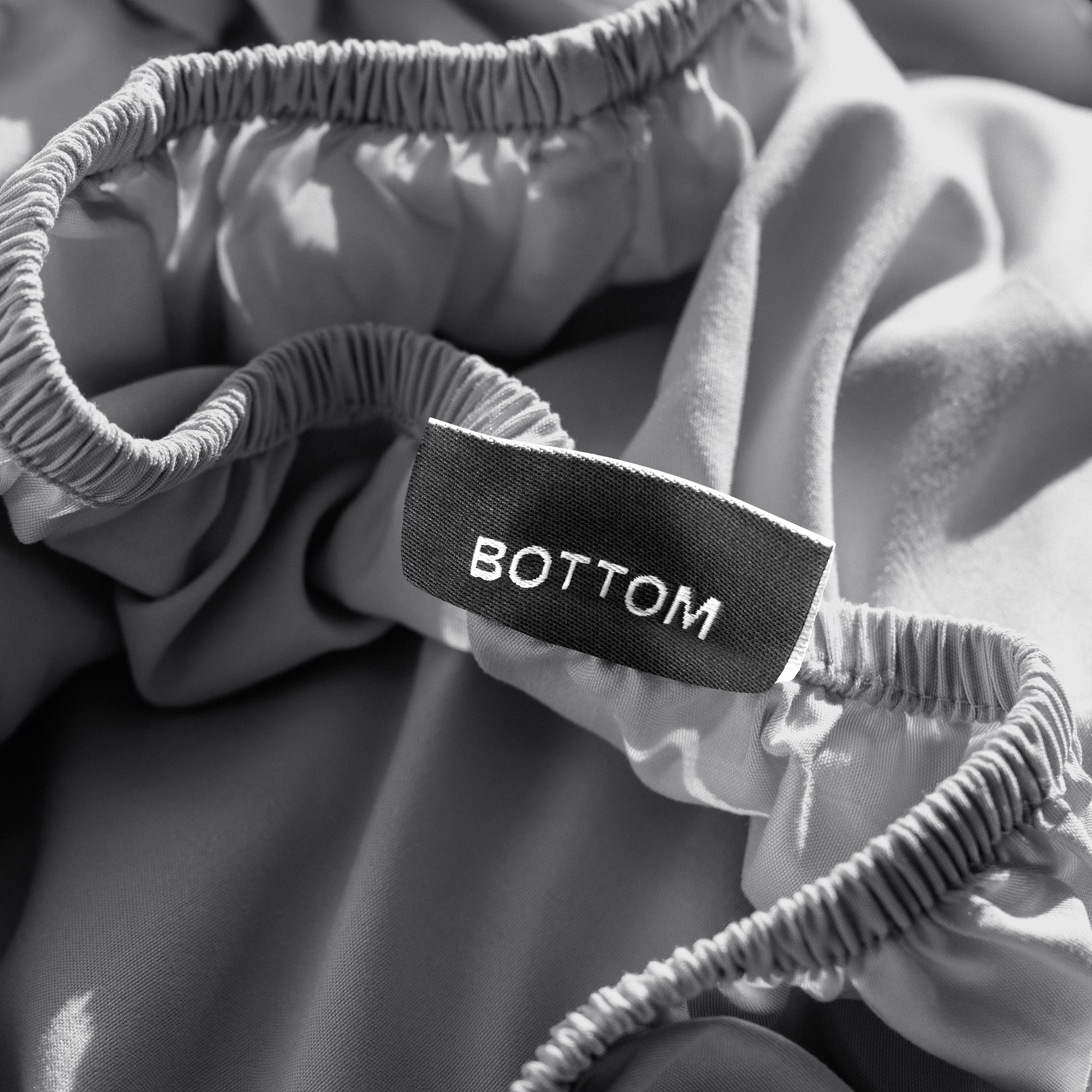 A close-up of a fitted sheet with a label printed with the word 'BOTTOM' in white.