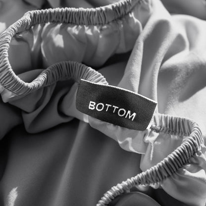 A close-up of a fitted sheet with a label printed with the word 'BOTTOM' in white.